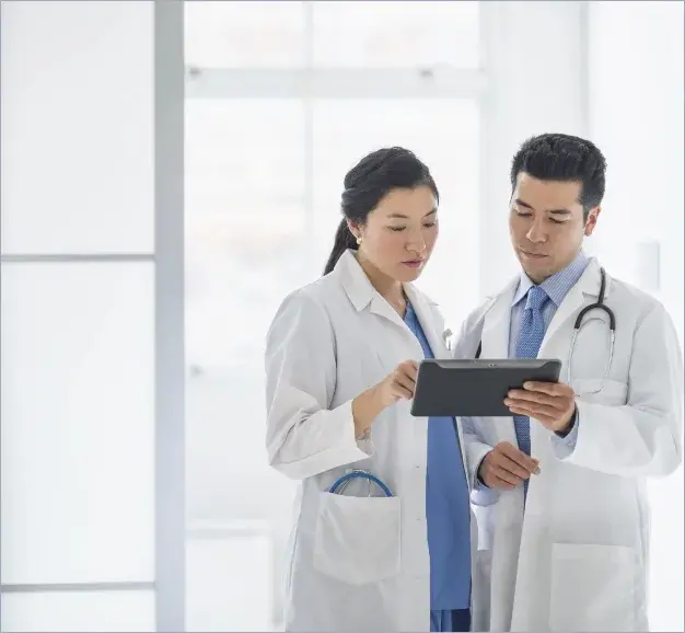 Two doctors, standing next to each other while collaborating on a tablet computer